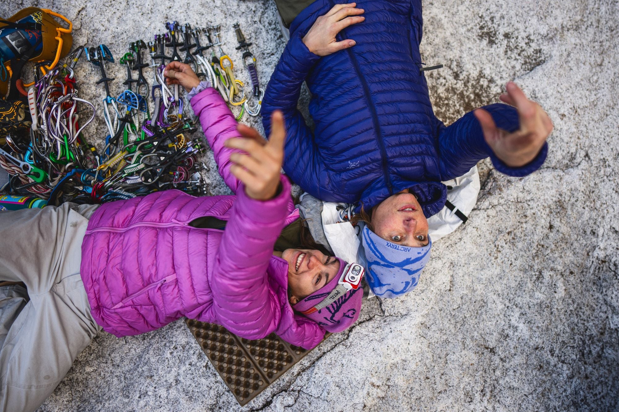 Two climbers in colorful jackets on a rocky surface with climbing gear.