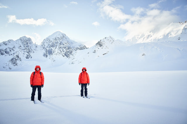two people stand on the snow wearing Alpha Parka